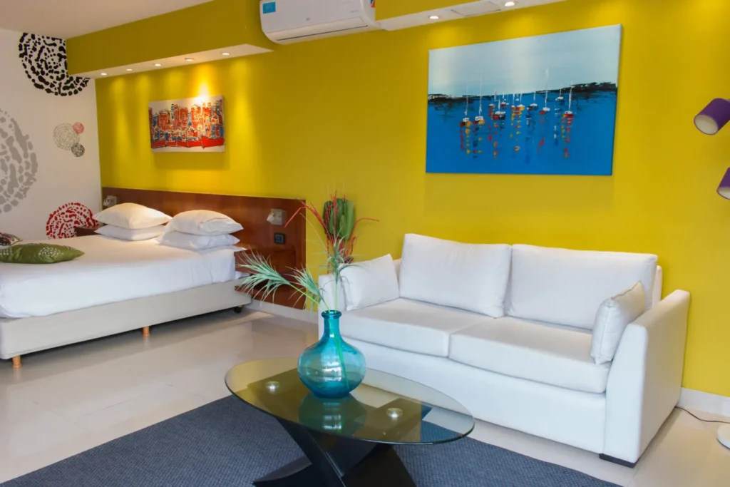 Living area with white sofa, glass coffee table and turquoise vase on a yellow wall