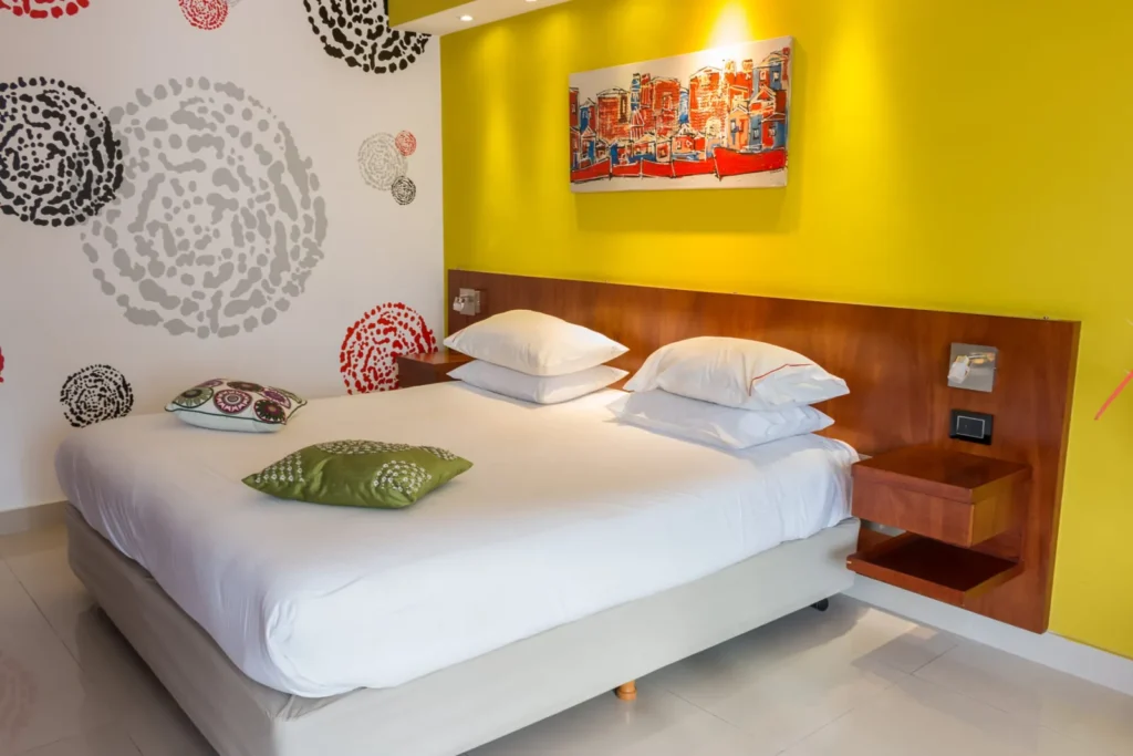 Bed with wooden headboard against a yellow wall in the Superior Room with Balcony