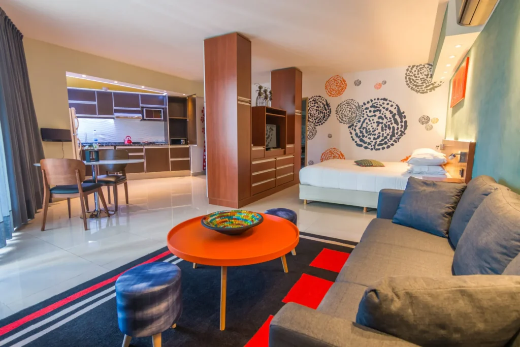 Habitación Superior con balcón: cama, sillón y cocina integrada con mesa naranja