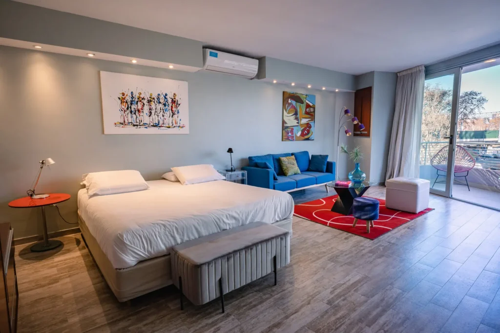 Habitación Superior con cama, sillón azul y balcón luminoso